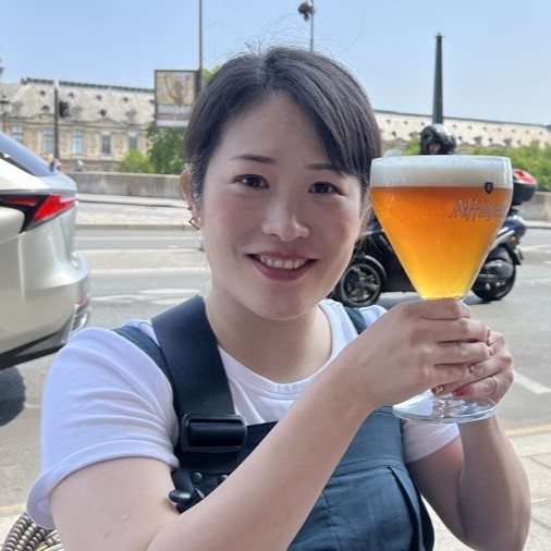 永川氏の顔写真。女性が顔の大きさ程のビールを、顔の横で両手で持って笑顔で写っている。